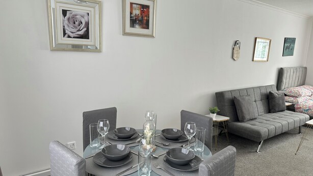 A dining area with a round table set for four, grey upholstered chairs, and a grey sofa in the background.
