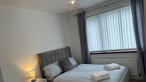 A modern bedroom with a bed, bedside table, lamp, and window with curtains.