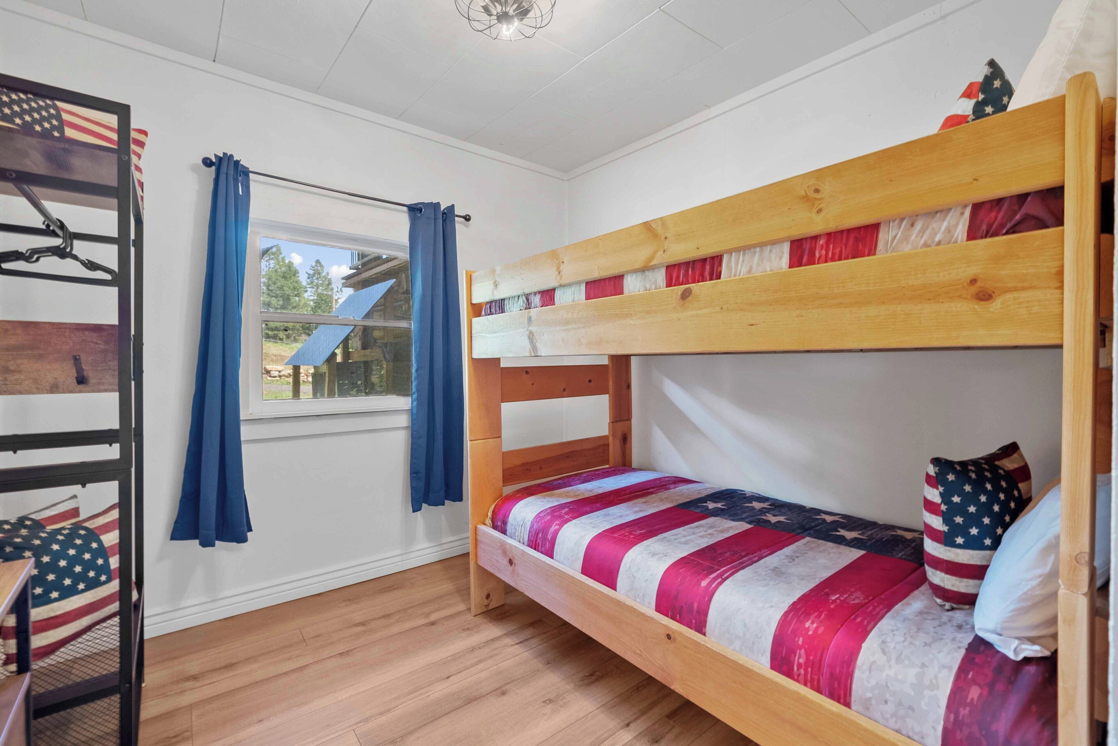 A bunk bed room with a window, curtains, and a view of a house.