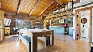 A spacious room with a pool table, wooden flooring, a loft area with a staircase, and a kitchen with blue cabinets and a red appliance. - Renovated Historic Flagstaff Cabin, Trails, Hot tub  (Flagstaff)