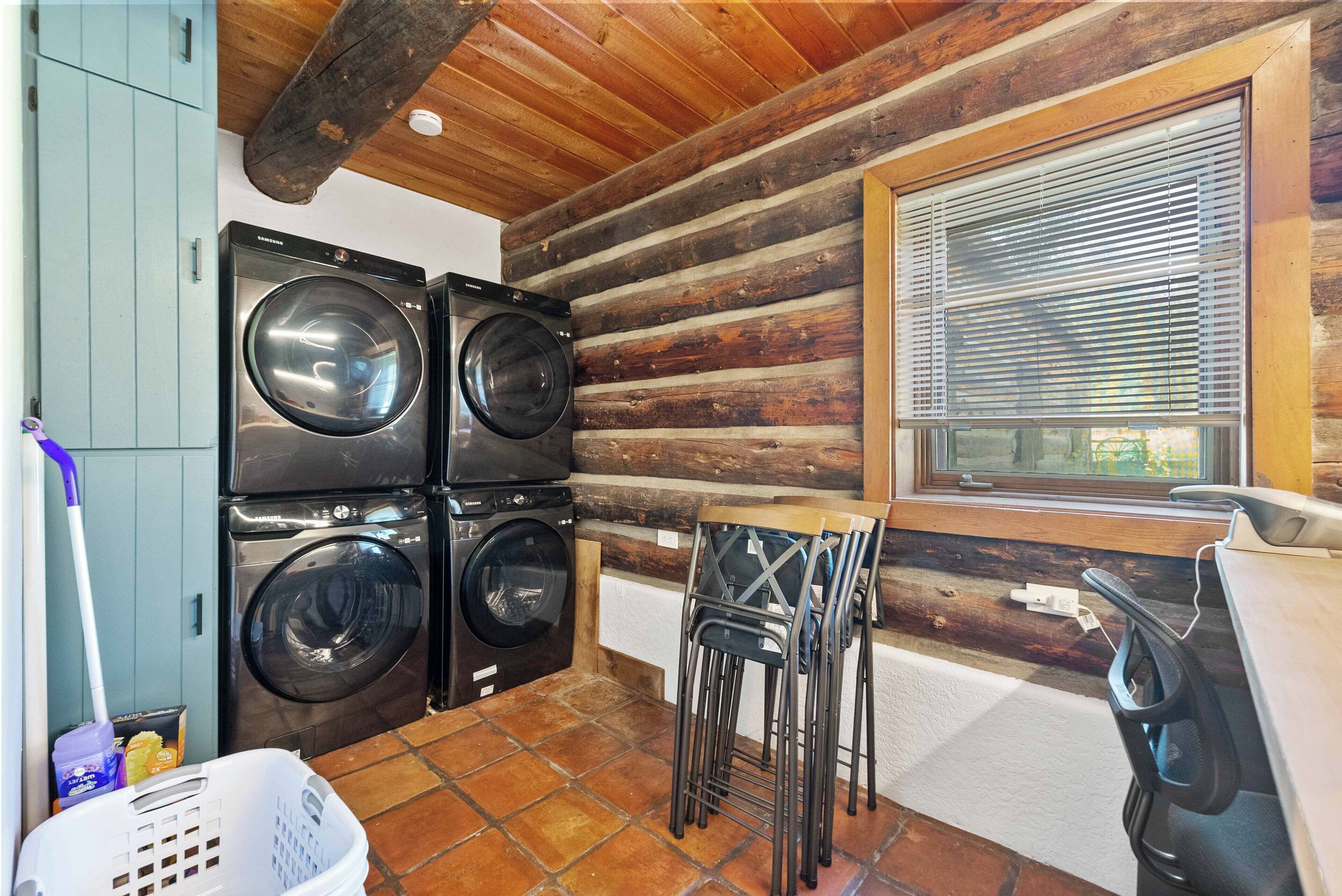 A laundry area with stacked washers and dryers, a window with blinds, and a chair near the window.