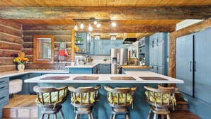 A rustic kitchen with wooden beams, a central island with stools, and blue cabinetry. - Renovated Historic Flagstaff Cabin, Trails, Hot tub  (Flagstaff)