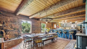 A rustic wooden cabin interior with a stone fireplace, a long dining table, and a bar area with stools. - Renovated Historic Flagstaff Cabin, Trails, Hot tub  (Flagstaff)
