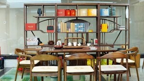 A dining area with a glass-top table, wooden chairs, and a decorative metal partition with books and boxes.