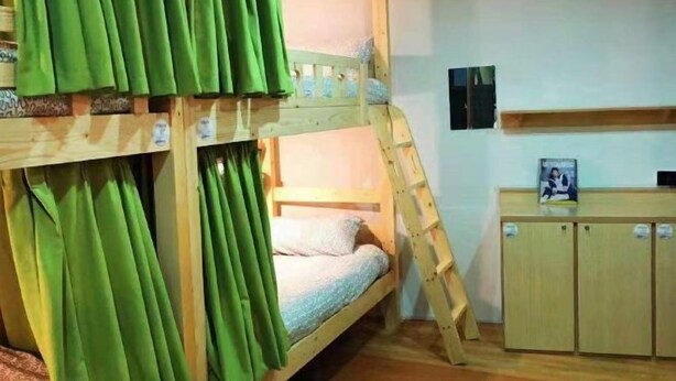 A bunk bed room with green curtains, a wooden desk, and a small cabinet.