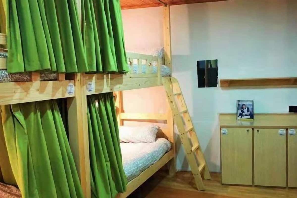 A bunk bed room with green curtains, a wooden desk, and a small cabinet.