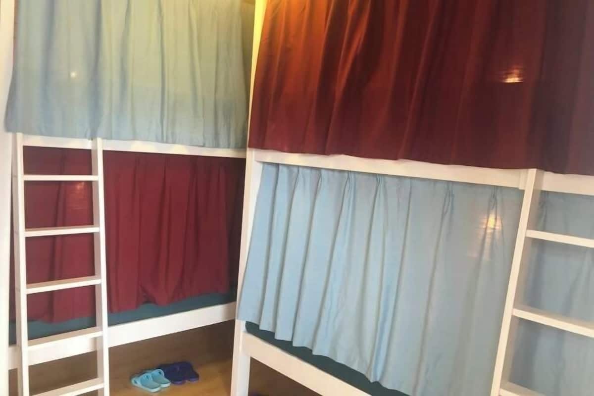 A bunk bed with a ladder on the left, a lower bunk with a red curtain, and a top bunk with a light blue curtain.