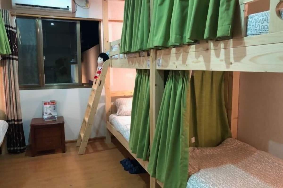 A bunk bed room with green curtains, a small wooden stool, and a window.