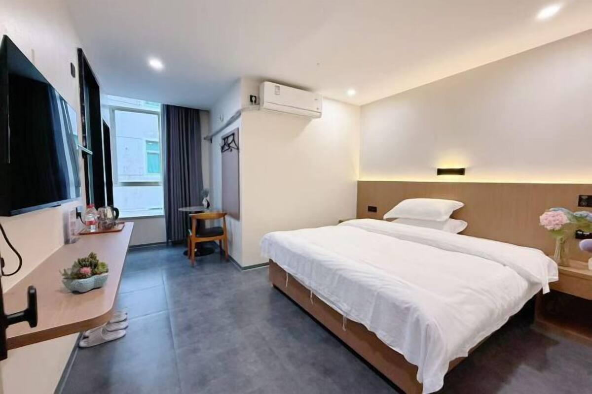 A hotel room with a bed, a desk, a chair, an air conditioning unit, and a television.