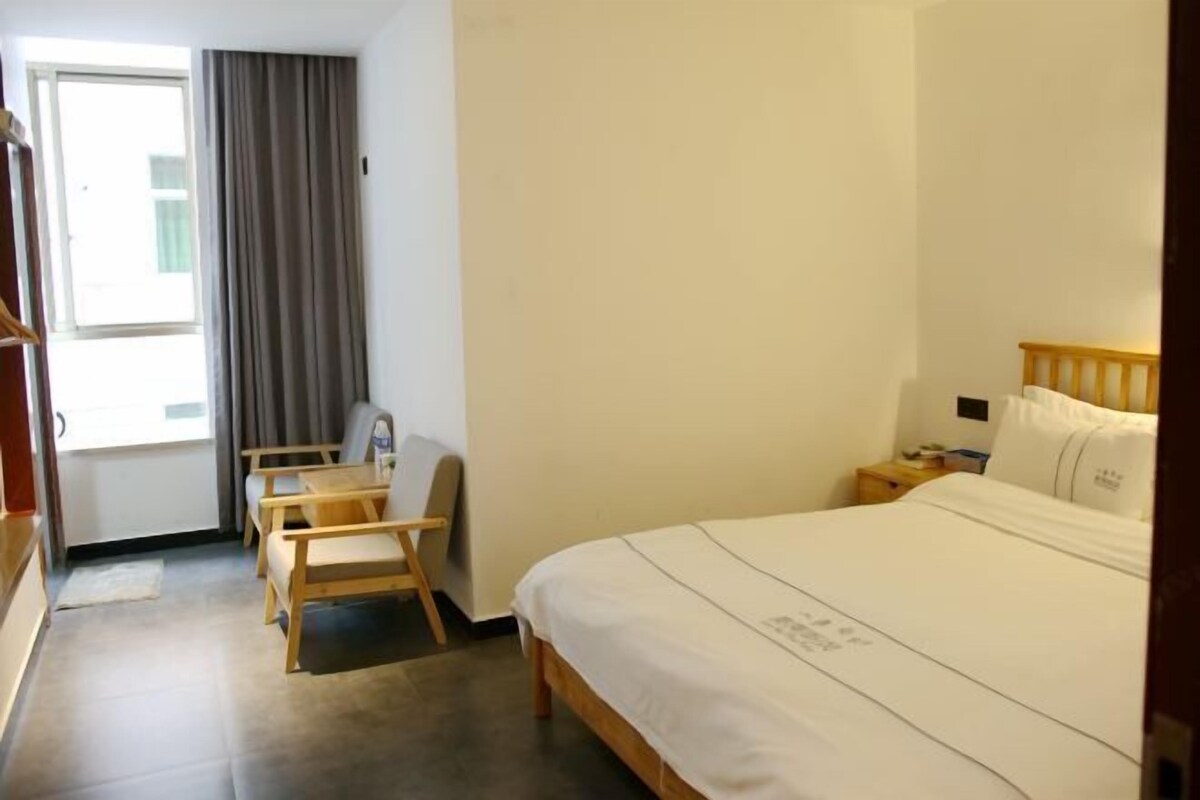 Una habitación de hotel con cama, escritorio, silla y ventana con cortinas.