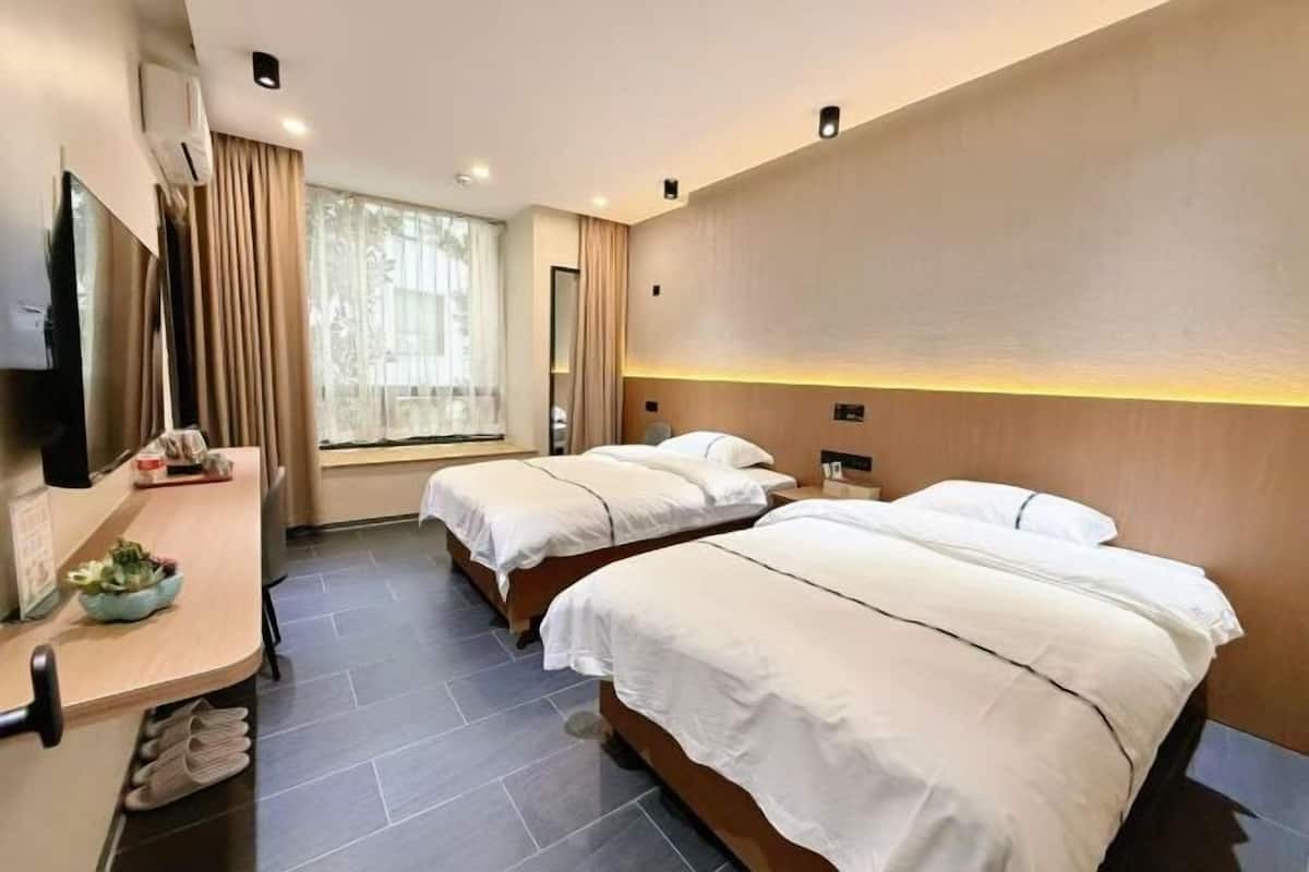 A hotel room with two beds, a desk with a chair, a TV, and a window with curtains.