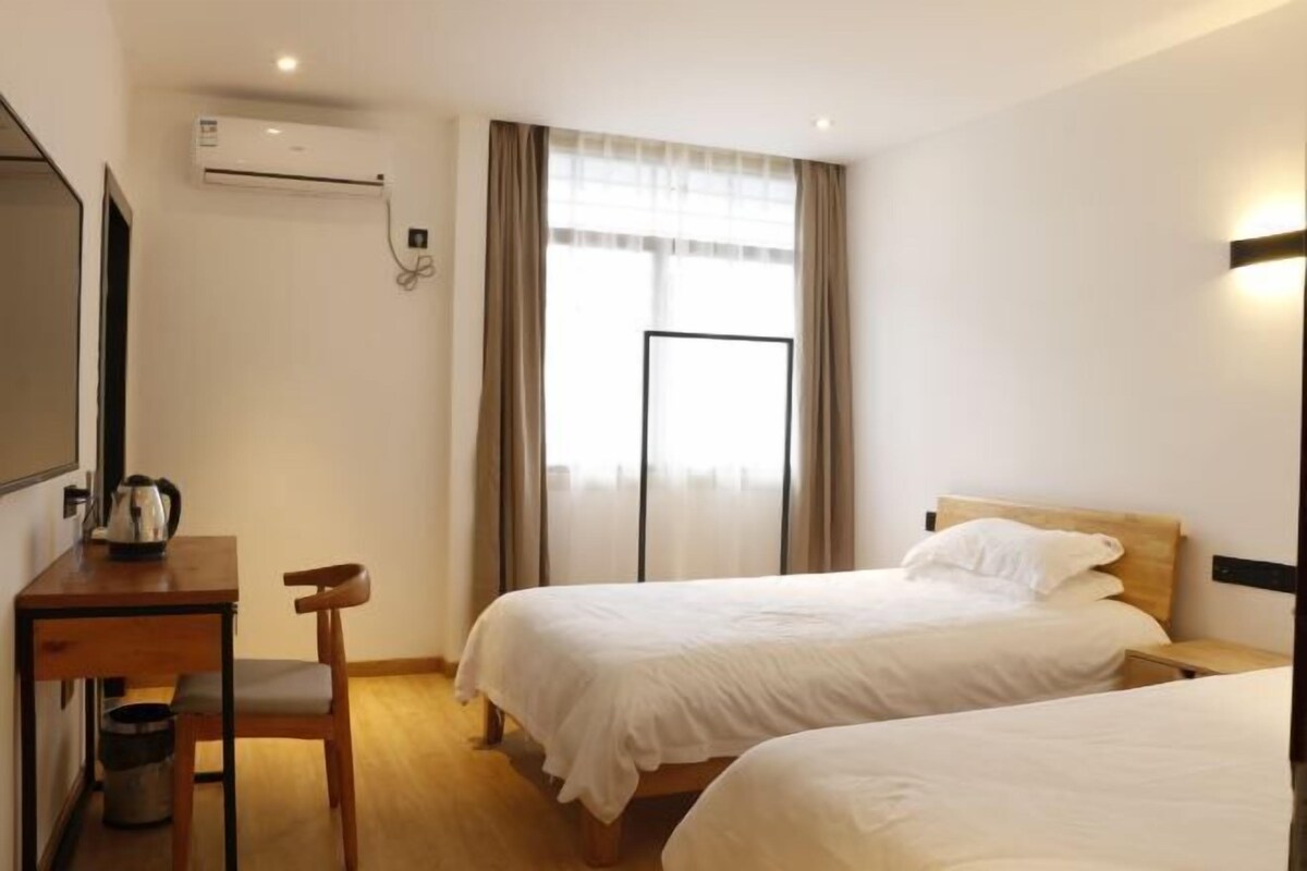 Habitación de hotel con dos camas, un escritorio con silla, cafetera y aire acondicionado.
