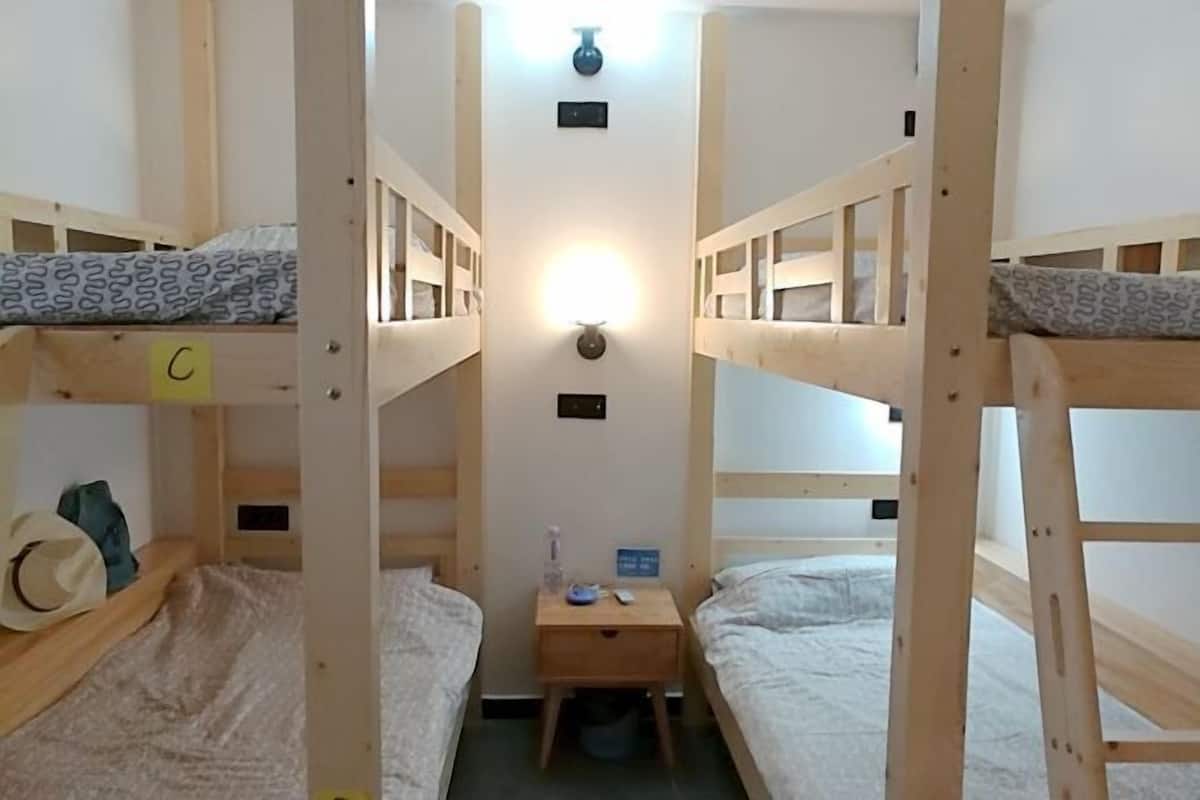 A bunk room with wooden bunk beds, a nightstand with a lamp, and a small table with a bottle and a remote control.