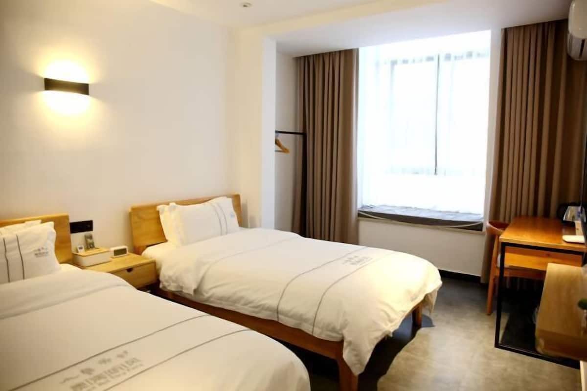 A hotel room with two beds, a desk, a chair, a nightstand, and a window with curtains.