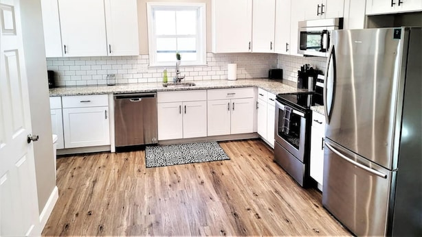 A modern kitchen with white cabinets, a stainless steel refrigerator, a microwave, and a dishwasher.
