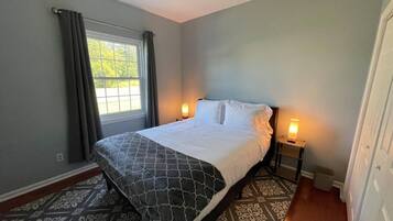 A bedroom with a bed, two bedside lamps, a window with curtains, and a patterned carpet.