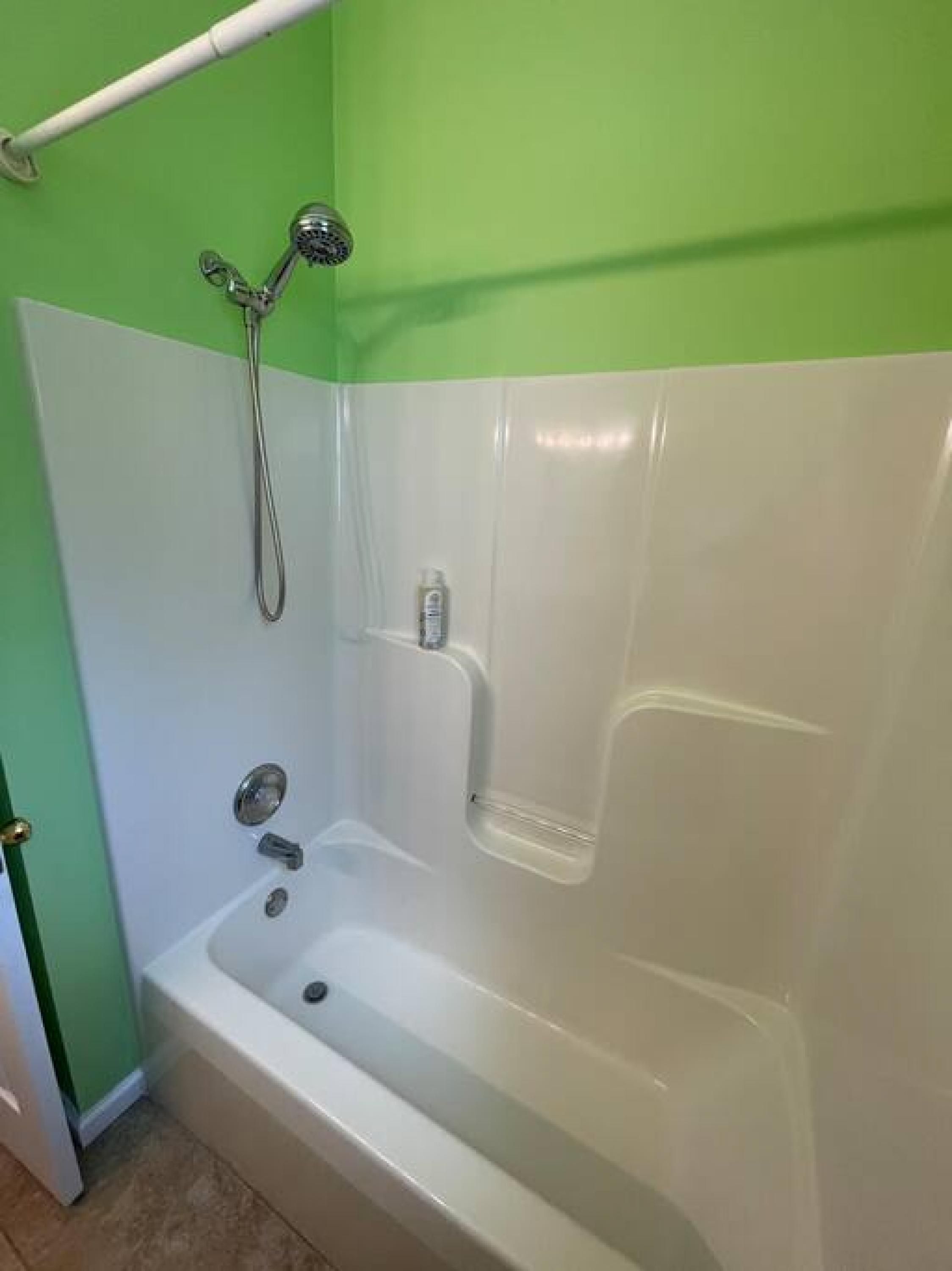 A bathroom with a bathtub, shower, and a green and white color scheme.