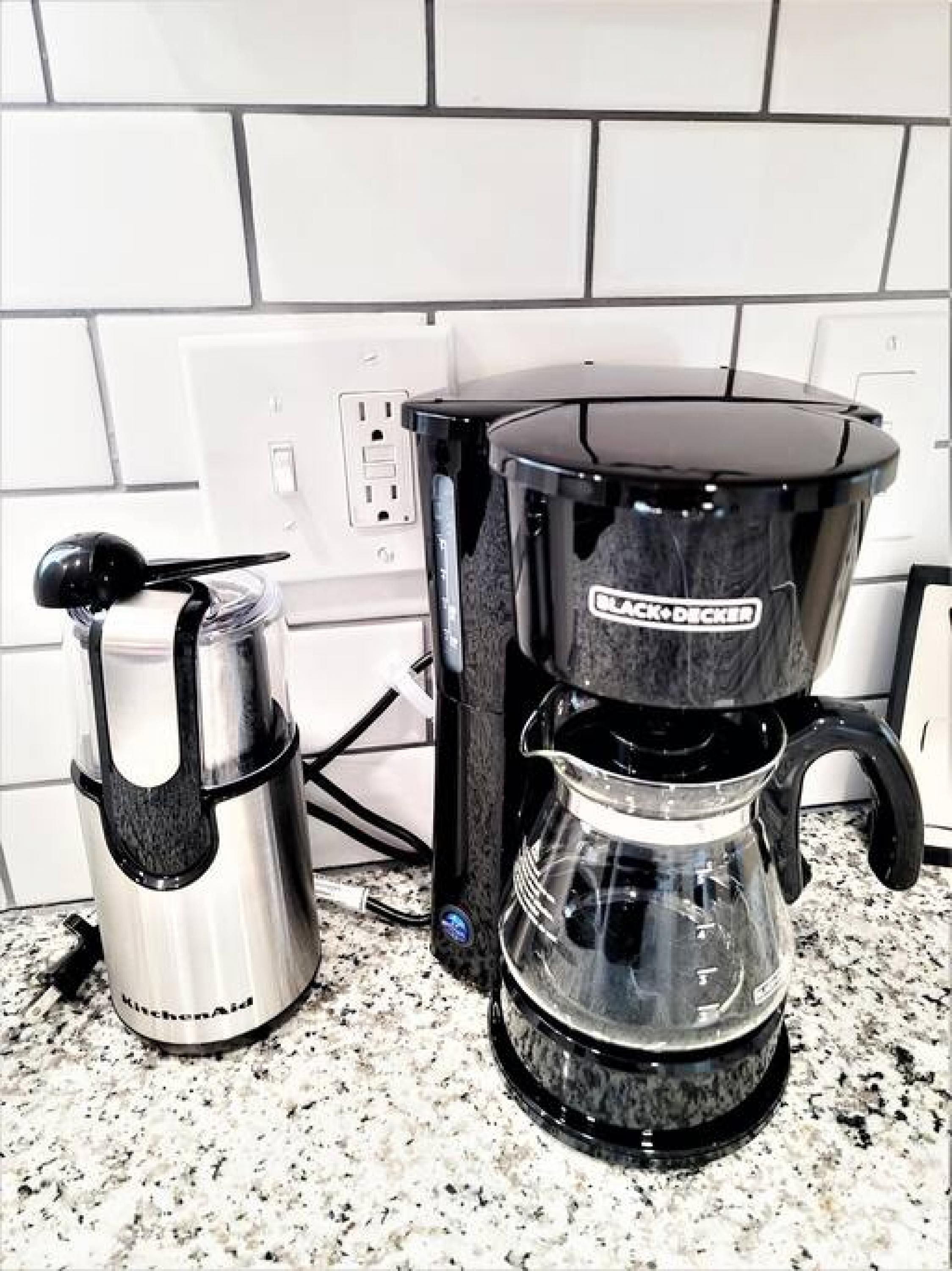 A kitchen with a coffee maker, a kettle, and a coffee pot on a granite countertop.