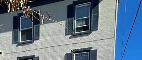 Un edificio de dos pisos con fachada de ladrillo y múltiples ventanas, incluyendo una puerta con una placa numérica.