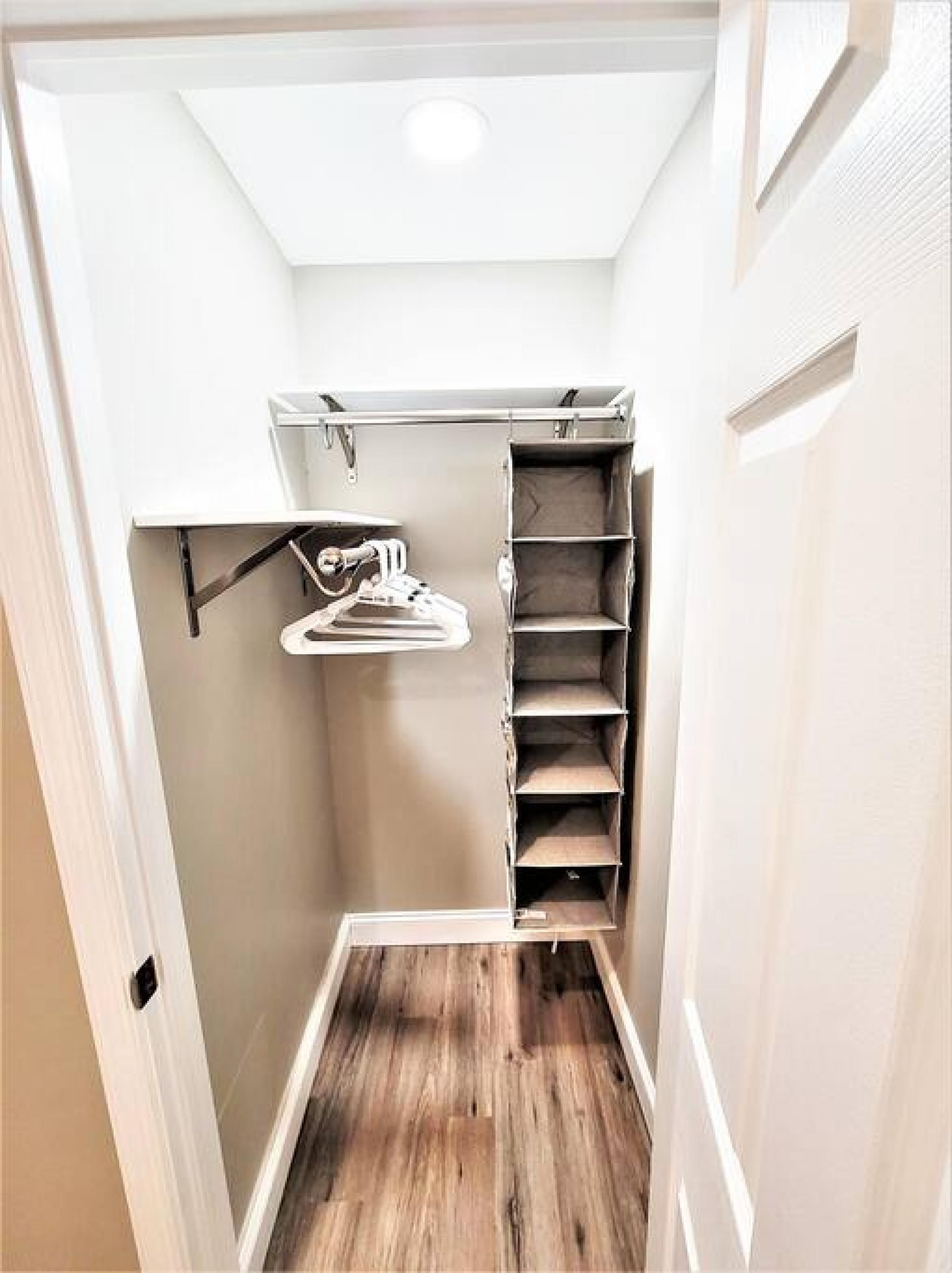 A narrow hallway with a wooden floor, a white door on the left, and a closet with shelves and hanging space on the right.