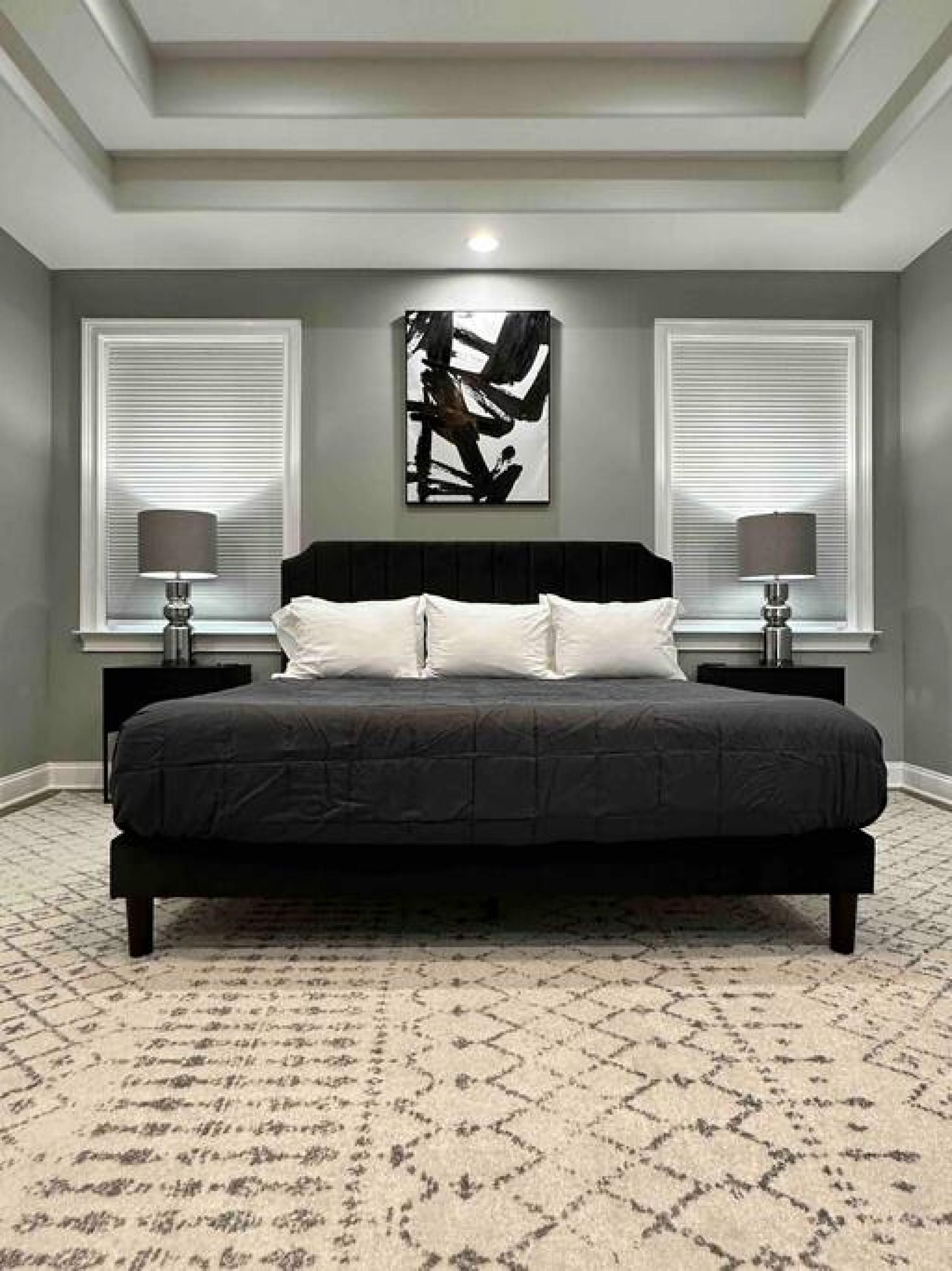 Ein Schlafzimmer mit einem großen Bett, zwei Nachttischen, einem an der Wand hängenden abstrakten Gemälde und einem gemusterten Teppich.