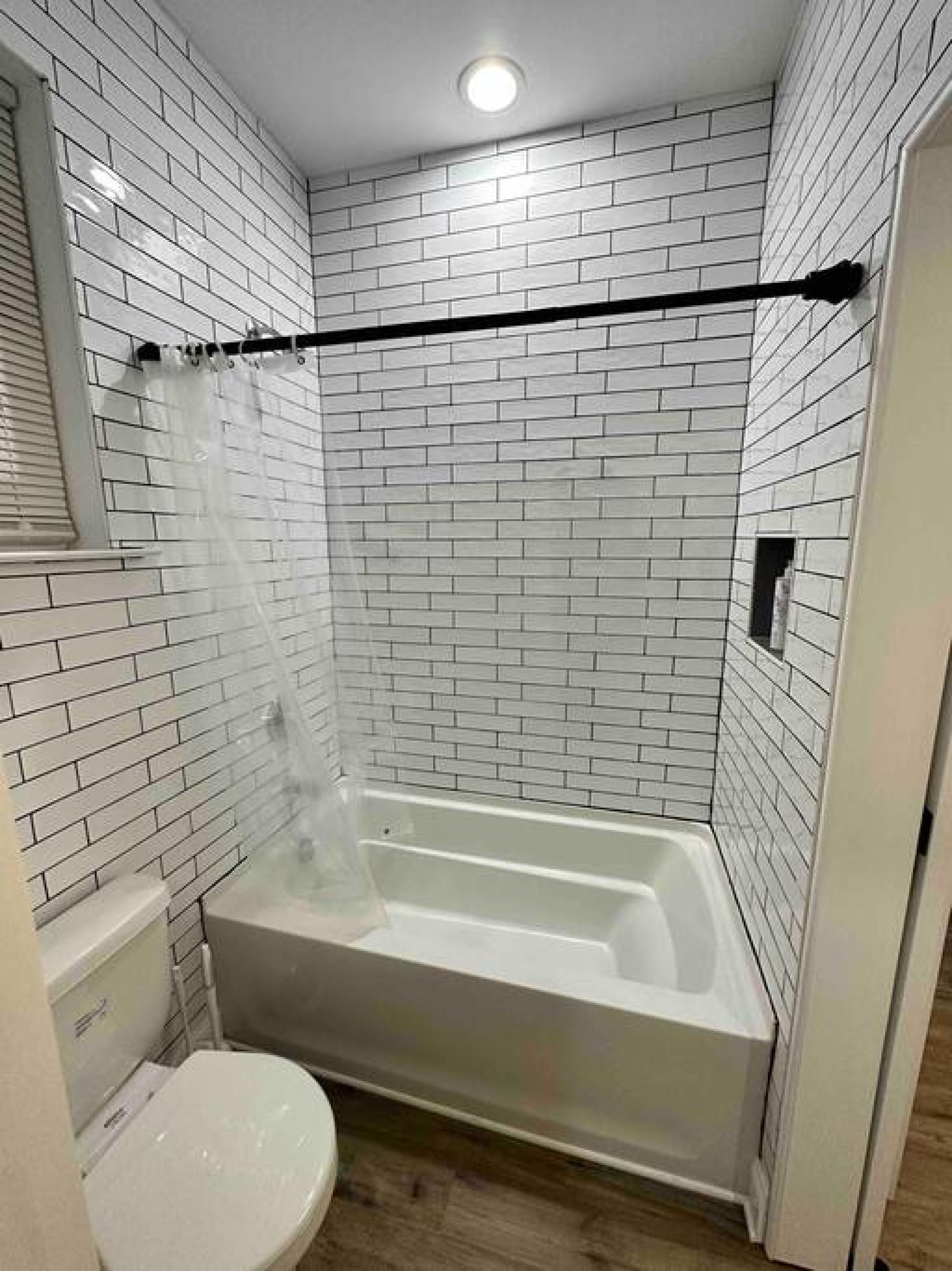 A bathroom with white subway tile walls, a white bathtub, and a white toilet.