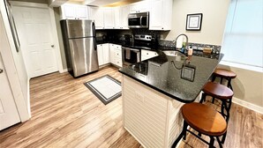 A modern kitchen with white cabinets, stainless steel appliances, a black countertop, and a window with blinds. - Boardwalk- Large Modern Unit With King bed Fast Wifi Free Coffee and Easy Parking (Wilmington)