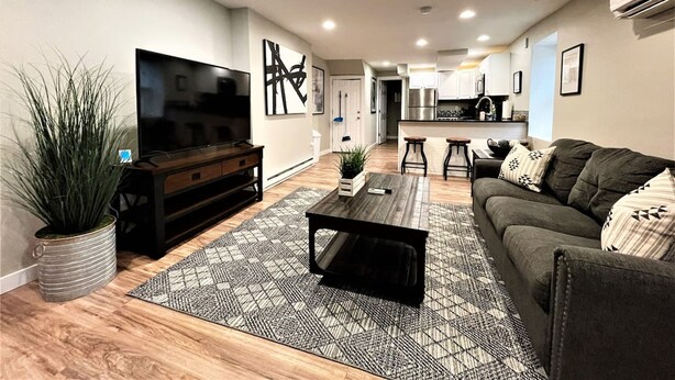 A modern living room with a flat-screen TV, dark sofa, and a coffee table. There is a kitchen in the background with white cabinets and stainless steel appliances. - Boardwalk- Large Modern Unit With King bed Fast Wifi Free Coffee and Easy Parking (Wilmington)