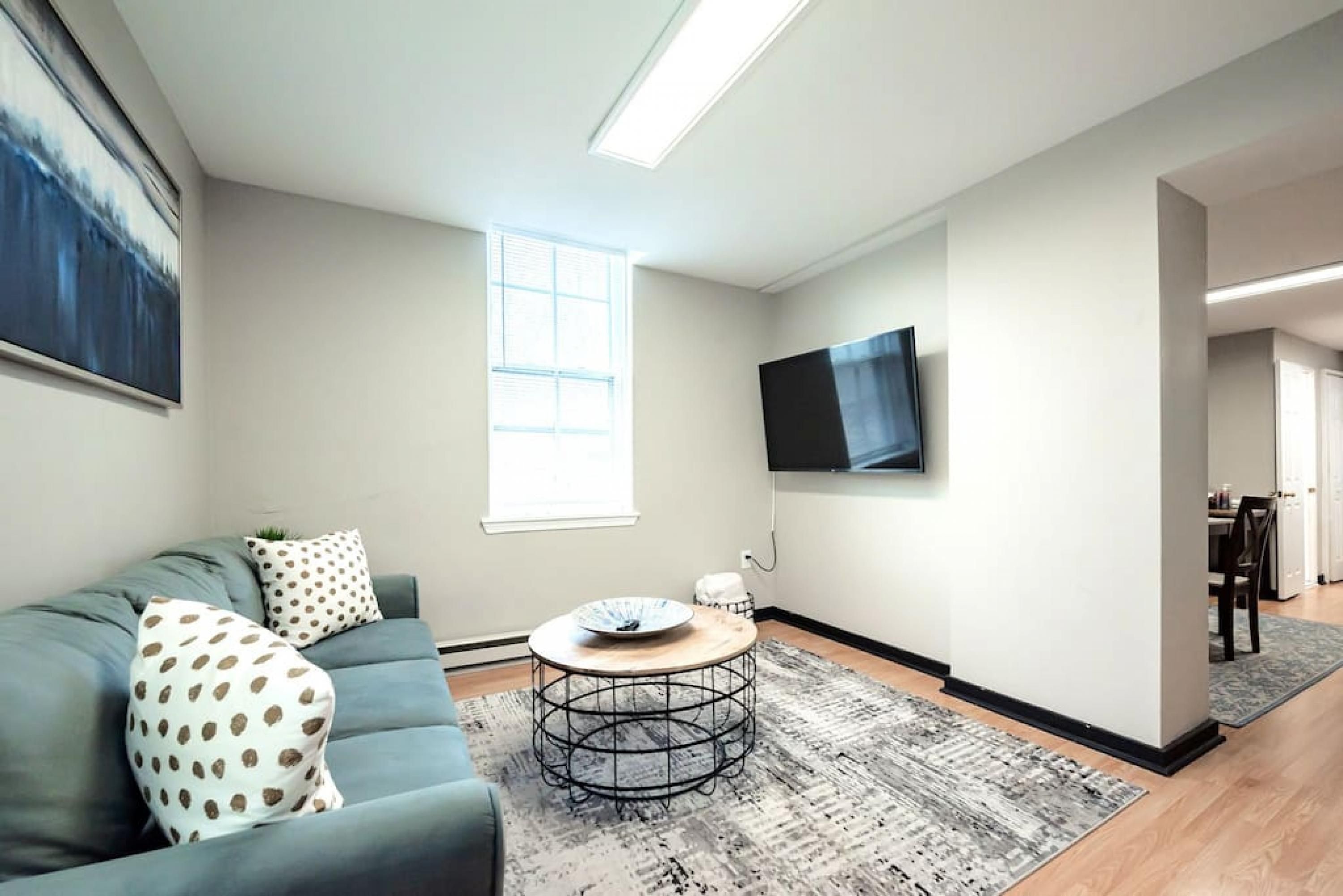 Un salon moderne avec un canapé gris, une table basse ronde et un téléviseur à écran plat fixé au mur.