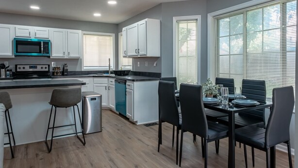 Una cocina moderna con armarios blancos, microondas integrado y comedor con cuatro sillas negras y una mesa preparada para cuatro personas.
