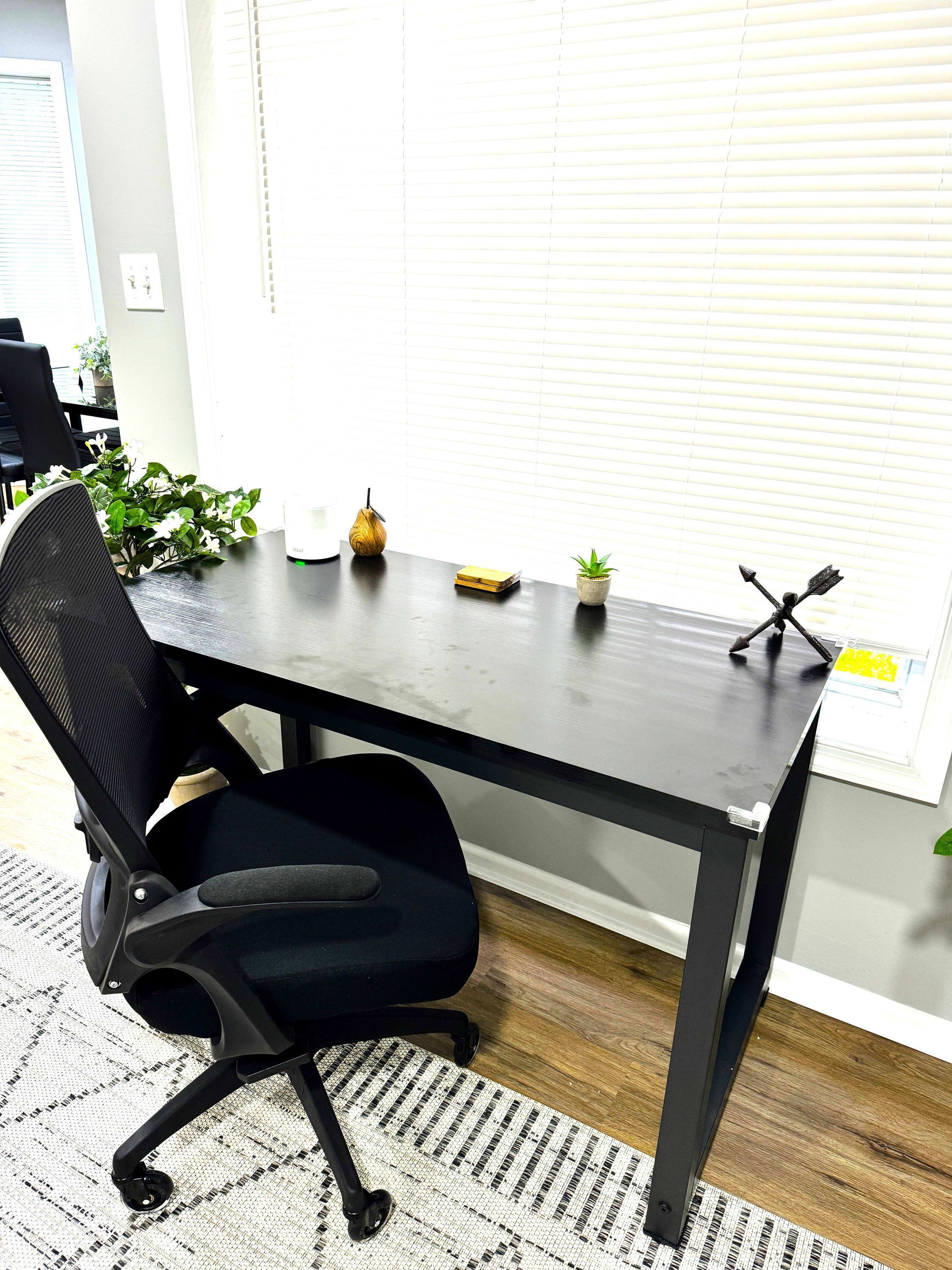 A modern office desk with a black chair, a small potted plant, a decorative item, and a window with blinds.