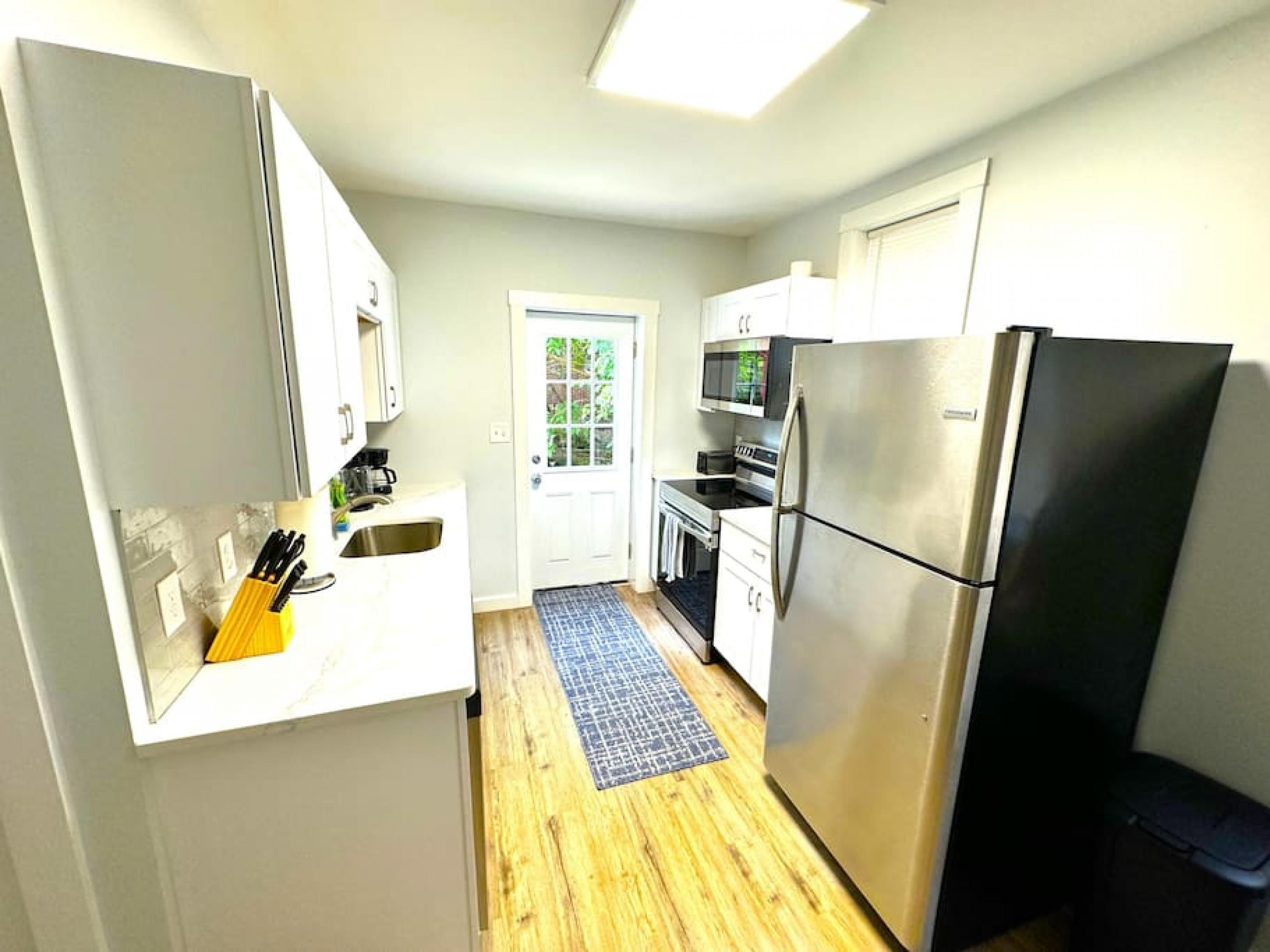 A compact kitchen with white cabinets, a stainless steel refrigerator, a microwave, and a sink.