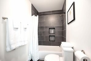 A modern bathroom with a bathtub, toilet, and shower.