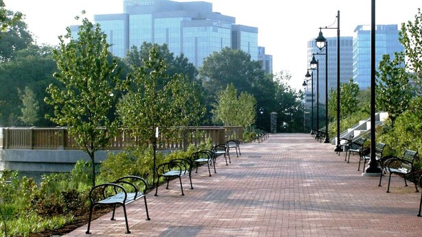 A paved pathway with benches and trees, leading towards a modern building with glass windows. - Park Place- Cozy Modern Space Fully Updated Fast Wifi Good Coffee and Easy Parking (Wilmington)
