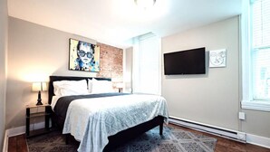A bedroom with a bed, a nightstand, a lamp, a painting, a TV, and a patterned rug. - Park Place- Cozy Modern Space Fully Updated Fast Wifi Good Coffee and Easy Parking (Wilmington)