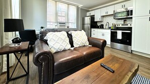 Ein Wohnzimmer mit braunem Ledersofa, einem Holztisch und einer Fernbedienung.