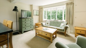 A living room with a television, a sofa, a coffee table, and a dresser. - Cotteswold House (Cirencester)
