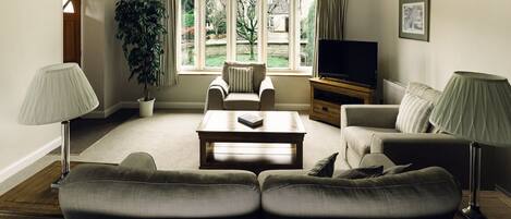 A living room with a sofa set, a coffee table, a TV stand, and a large window with curtains.