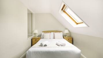 A neatly arranged bedroom with a bed, two bedside tables, a nightstand, and a skylight.