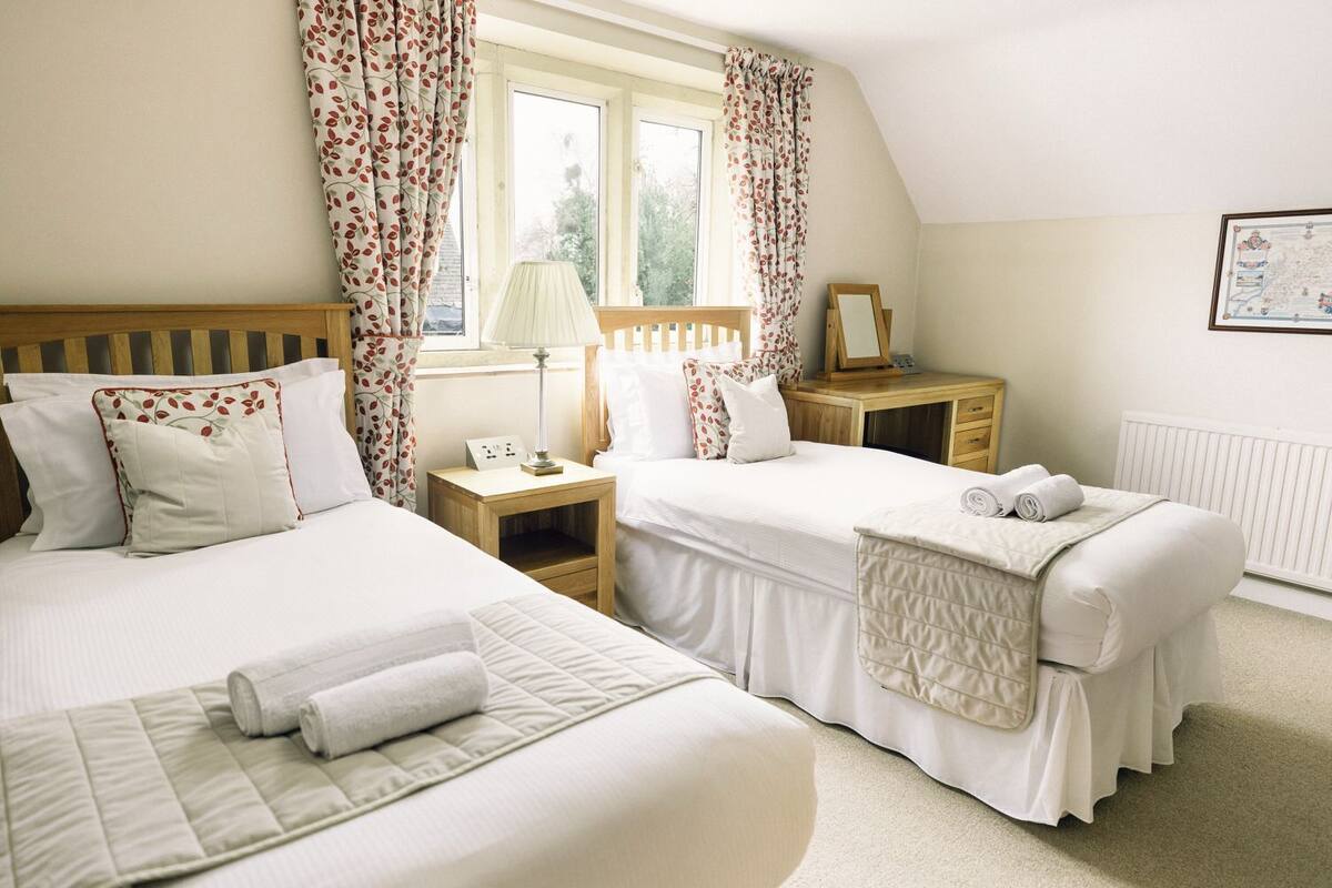 A bedroom with two beds, a wooden headboard, a nightstand with a lamp, and a framed picture on the wall.