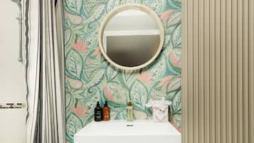 Un baño con ducha, lavamanos y artículos de aseo, y un espejo.