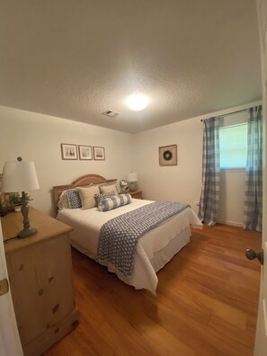 A bedroom with a bed, wooden dresser, and a window with curtains.