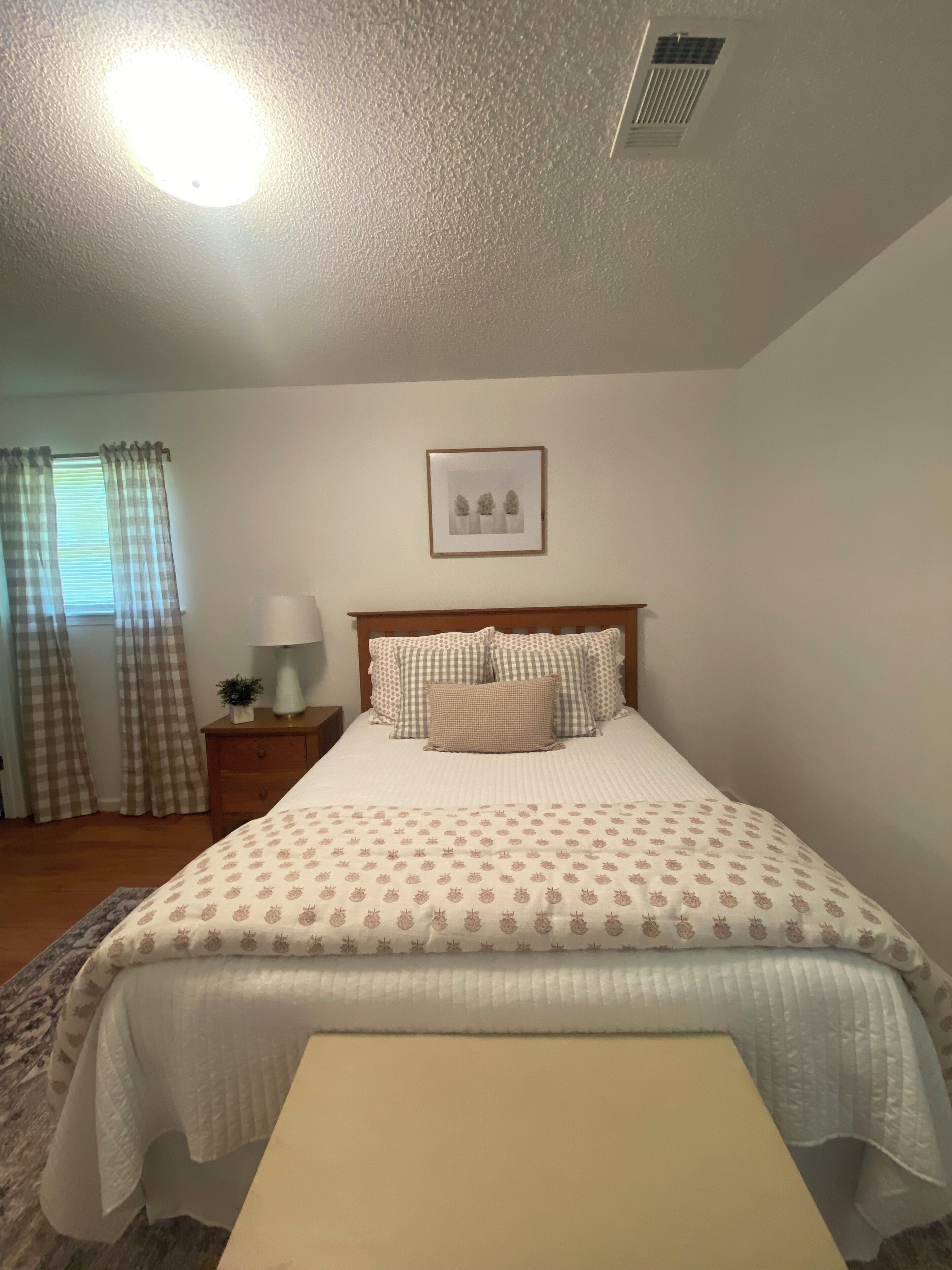 A neatly made bed with a patterned bedspread, a bedside table with a lamp, and a framed picture on the wall.