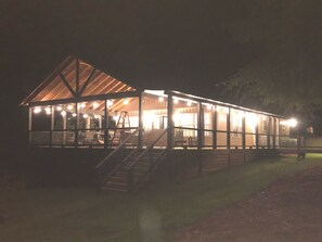 A large, well-lit wooden structure with a covered patio area, a staircase leading to an upper level, and a ladder against the wall.