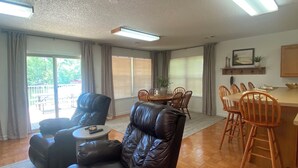 A spacious living room with a leather sofa, dining area with wooden chairs, and large windows with blinds. - Waterfront cabin on Lake Martin near restaurants, golf and, AU football (Dadeville)