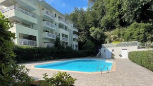 Une piscine dotée d’une terrasse carrelée, entourée de verdure et bordée d’un immeuble à plusieurs étages avec des balcons.