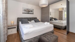 A modern bedroom with a large bed, a bedside table, a mirror, and a hanging light fixture.