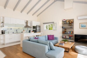 Um espaço de estar moderno com cozinha, sofá, mesa de centro e estante.
