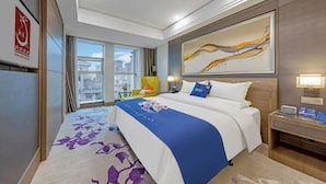 Habitación de hotel con una cama grande, vistas a la ciudad, una obra de arte moderno y un escritorio con lámpara.