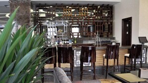 Un área de bar moderna con un diseño geométrico único en la pared, taburetes y un espacio de estar con sofá y sillas.
